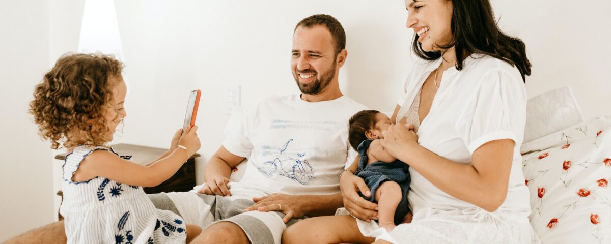 Família com 2 filhos usando smartphone na cama e brincando junto