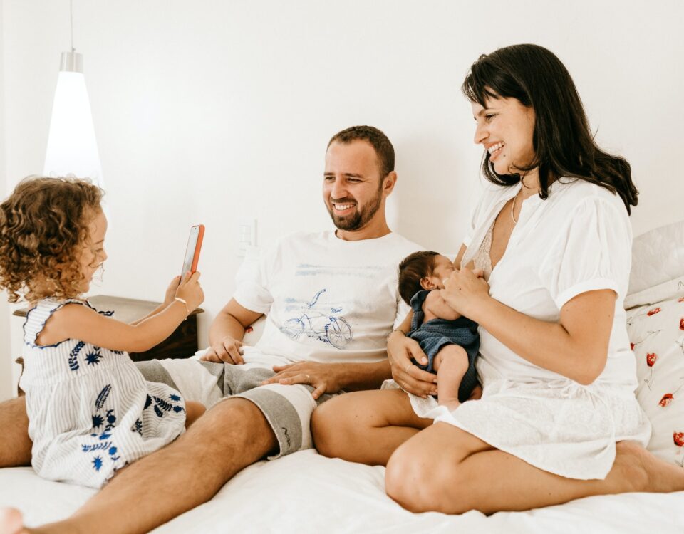 Família com 2 filhos usando smartphone na cama e brincando junto
